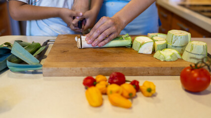 close up of the hands of a woman and her son cutting a leek with a knife on a board