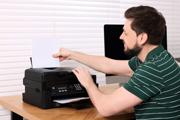 Man using modern printer at wooden table indoors
