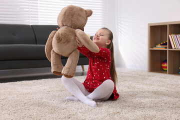 Cute little girl playing with teddy bear at home
