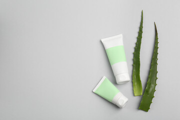 Tubes of toothpaste and fresh aloe on light grey background, flat lay. Space for text