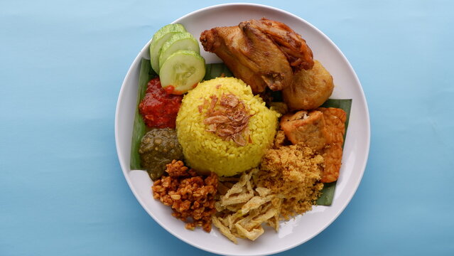 Nasi Kuning or Yellow rice with traditional fried chicken, tofu, tempeh, and smashed potato on blue background. Indonesia food.