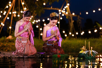 Two thai woman sitting wai on a raft by the river, Asian women in traditional Thai costumes bring...