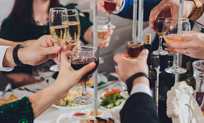 Close up shot of group of people clinking glasses with wine or champagne in front of bokeh...