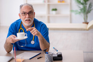 Old male doctor drinking coffee during break