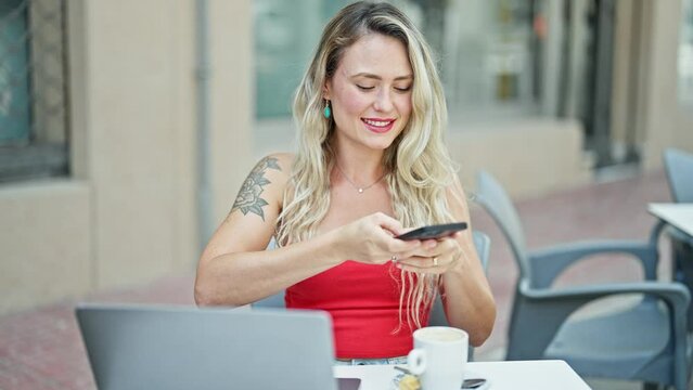 Young blonde woman make photo to coffee by smartphone sitting on table at coffee shop terrace