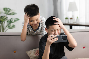 Asian boy playing games online with his smartphone, he mad feeling very angry on a sofa, games addict problem