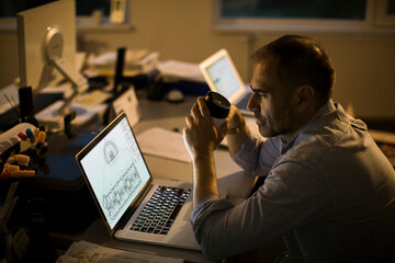Middle aged architect having coffee while going over building plans in the office working overtime...
