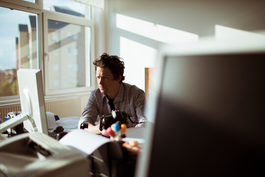 Young photographer going through his camera at his desk in the office office - Powered by Adobe
