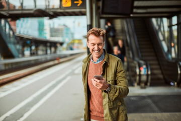 Middle aged man using a smartphone while waiting for a train at the train station