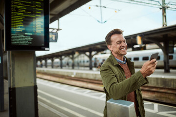 Middle aged man using a smartphone while waiting for a train at the train station