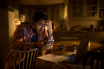Young caucasian man going over his finances on the smart phone in the kitchen
