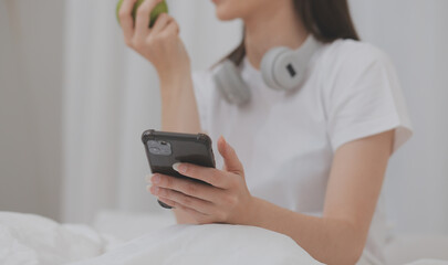 Efficient Young Millennial Girl Sitting on a Bed in the Morning, Uses Laptop Computer and Eats Croissants and Drinks Coffee for Breakfast