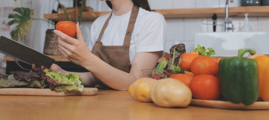 Delicious fruit and vegetables on a table and woman cooking. Housewife is cutting green cucumbers on a wooden board for making fresh salad in the kitchen.