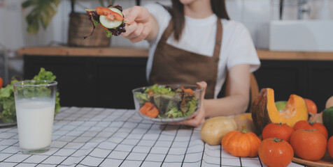 Delicious fruit and vegetables on a table and woman cooking. Housewife is cutting green cucumbers on a wooden board for making fresh salad in the kitchen.