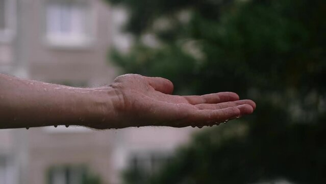 rain falls on a man hand against the background of houses in the city, a rainy day outdoors in a city park. close up. the hand catches raindrops.
