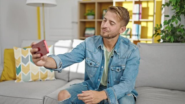 Young caucasian man taking selfie picture with smartphone sitting on the sofa at home