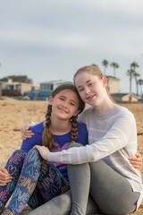Two fully clothed sisters sitting in the sand, on the sunset beach, California, USA, vertical