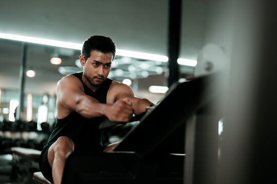 Motivated young asian sportsman having workout on rowing machine. Handsome man bodybuilder training body on modern block exercises in gym