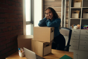 A young curly-haired logistics employee packs goods, collects parcels, puts things in a cardboard box, prepares a parcel for shipment, transports, sits on a windowsill and drinks a report in a book