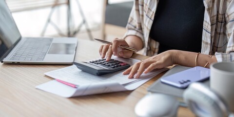 Young asian female work with financial papers at home count on calculator before paying taxes...