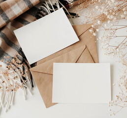 Cards mockup, envelopes, dried flowers and  plaid scarf top view on white background with copy...