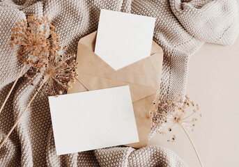 Cards mockup, envelopes, dried flowers and beige knitting plaid top view on beige background with copy space. flatlay. Blank, greeting card template.