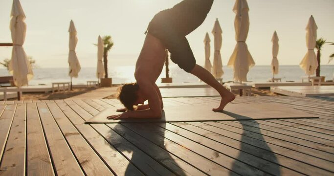 The guy stands on his head on a special mat on a sunny beach. Yoga classes