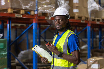 Male African American engineer holding walkie talkie and clipboard quality control standing at machine of factory warehouse. professional engineering machinery workshop.