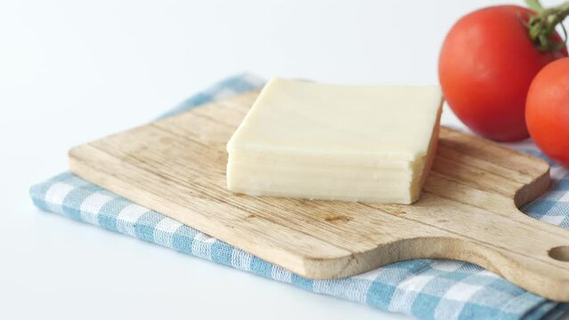 Slicing cheese into pieces and tomato on table 