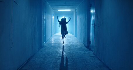 Little girl in white dress looking like a ghost carelessly running down the hallway of a haunted...