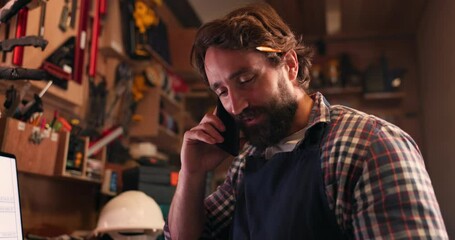 Phone call, manufacturing and a craftsman in a workshop for design, creative carpentry or artisan work. Mobile, contact and conversation with a carpenter, engineer or designer in his diy studio