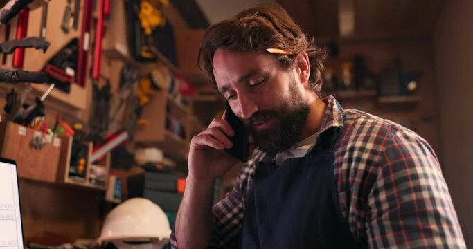 Phone call, manufacturing and a craftsman in a workshop for design, creative carpentry or artisan work. Mobile, contact and conversation with a carpenter, engineer or designer in his diy studio