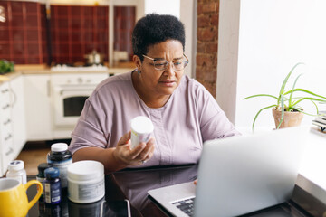 Horizontal image of black african american overweight elderly woman in spectacles holding bottle of...