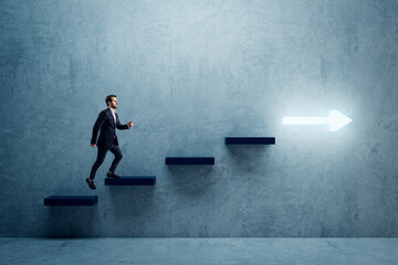 Side view of young business man climbing illuminated arrow stairs to success on concrete wall...