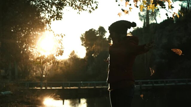 People enjoying having fun in autumn season at the park. One happy overjoyed woman throwing leaves in the air and outstretching ars with big smile expression on face. Natural lifestyle lady enjoy life