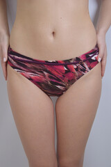 Women's swimming suit. Burgundy plum bikini bottoms with an abstract color pattern on the model. Women's clothing for the beach.