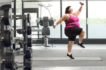 Fototapeta na wymiar Overweight woman exercising in a gym and jumping with weights