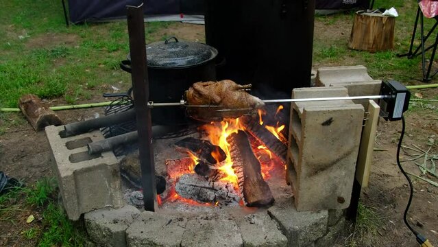 Slow motion of whole duck skewer onto automatic rotisserie being cooked over fire pit.
