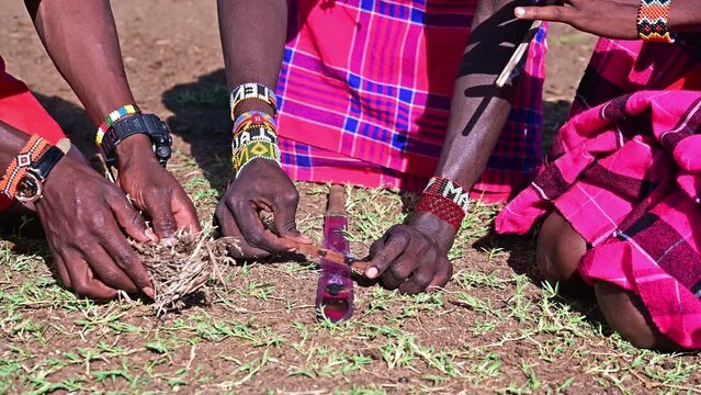 Several Maasai men light a fire in an ancient traditional way by rubbing dry twigs in a Maasai village in Kenya, Africa
