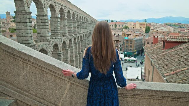 Beautiful tourist girl exploring Towering Roman Aqueduct of Segovia in SPAIN. A female tourist visiting and looking at Spanish Acueducto de Segovia in Castile and Le&oacute;n region, Spain
