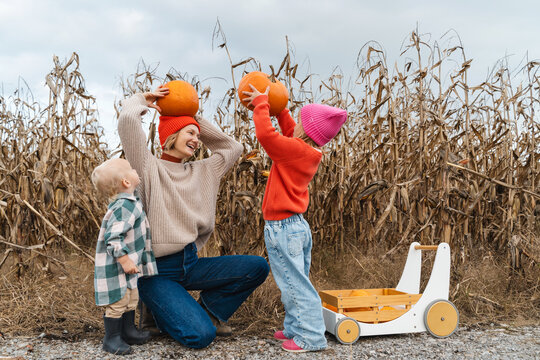 Mother with little children playing together in pumpkin patch.