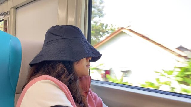 An Indonesian asian female train passenger is fall asleep near train window during sunny day while moving fast. Concept for Solo traveling, vacation, holiday, journey, trip. Railroad 4k footage