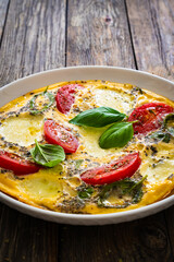 Omelette - scrambled eggs with mozzarella cheese and tomatoes on wooden table
