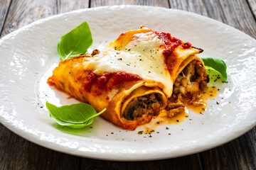Crepes stuffed with seared minced meat and mozzarella in tomato sauce on wooden table

