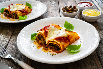Crepes stuffed with seared minced meat and mozzarella in tomato sauce on wooden table
