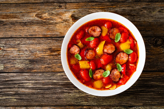 Delicious lecho - vegetables with sausages on wooden table
