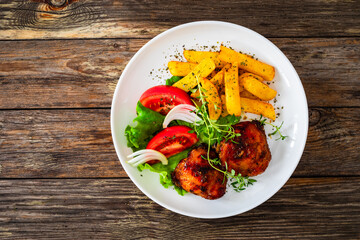Roasted chicken thighs with French fries and fresh vegetables on wooden table
