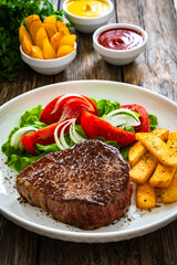 Grilled beef steak with French fries and fresh vegetables on wooden table
