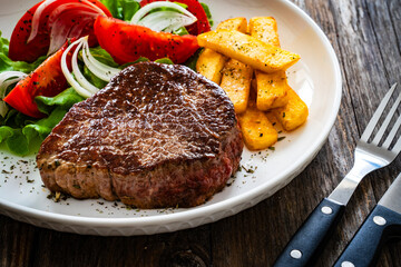 Grilled beef steak with French fries and fresh vegetables on wooden table
