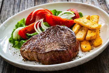 Grilled beef steak with French fries and fresh vegetables on wooden table
